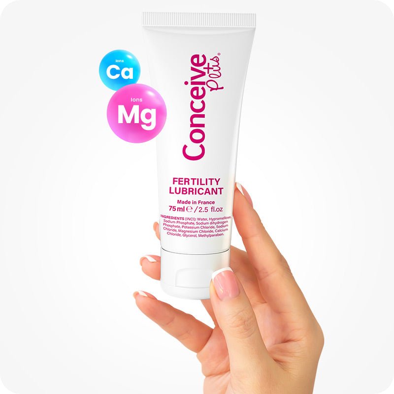 For Max Fertility Lubricant Bundle the image of a female hand holding tube of Conceive Plus Fertility Lubricant 75ml with fingers showing its front. There are two bubbles on the upper left corner of the tube with blue colored bubble having chemical symbol of Calcium as Ca and pink colored bubble having Magnesium symbol as Mg written in it. The woman hand has white nail polish on the tips of the nails.