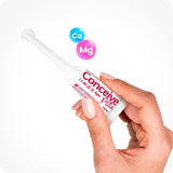 The image female right hand entering the frame from the bottom and holding a Conceive Plus Fertility Lubricant 3x4g pre-filled applicator with its front side towards the camera on a white background. There are two bubbles in the upper middle part of the frame just above the applicator with blue bubble has chemical formula of Calcium as 'Ca' and the pink bubble has the chemical formula of Magnesium as 'Mg' written inside them.